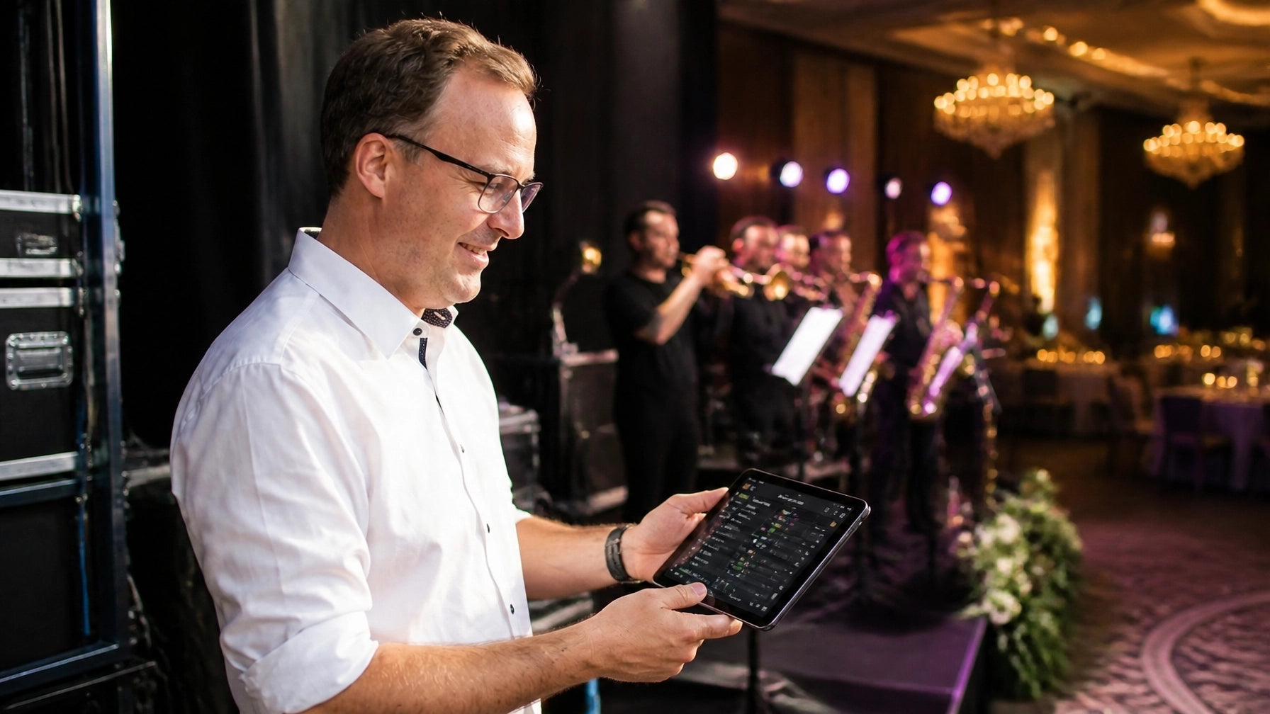 Reuben Avery reviewing musician confirmations backstage while a live band performs at an upscale event